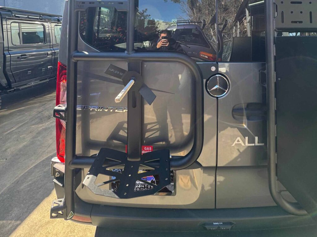 The driver-side ladder and tyre carrier assembly provides a rigid mounting point for a full-sized spare and stable roof access