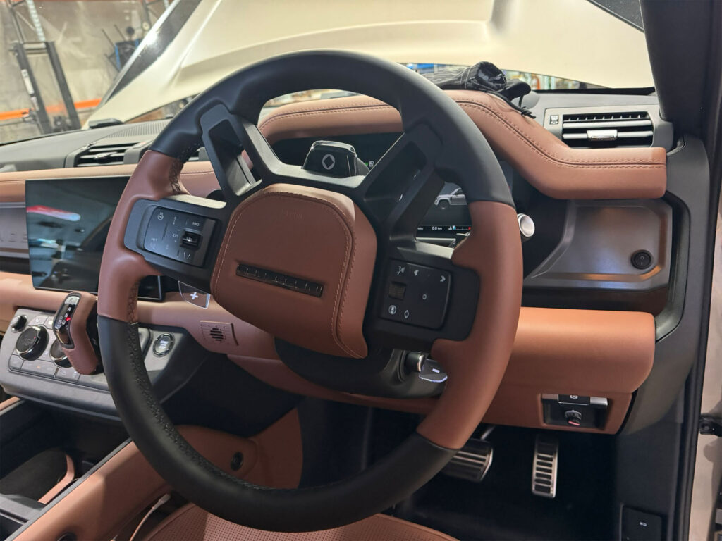 Driver's perspective of the Land Rover Defender steering wheel, showing the cleanly mounted auxiliary lightbar isolation switch on the right-hand side of the dashboard.