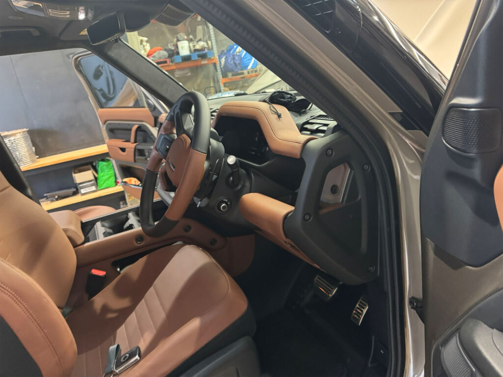 Wide view of the Land Rover Defender interior, displaying the premium brown leather seating and the discreetly mounted driving light switch on the lower dashboard panel.
