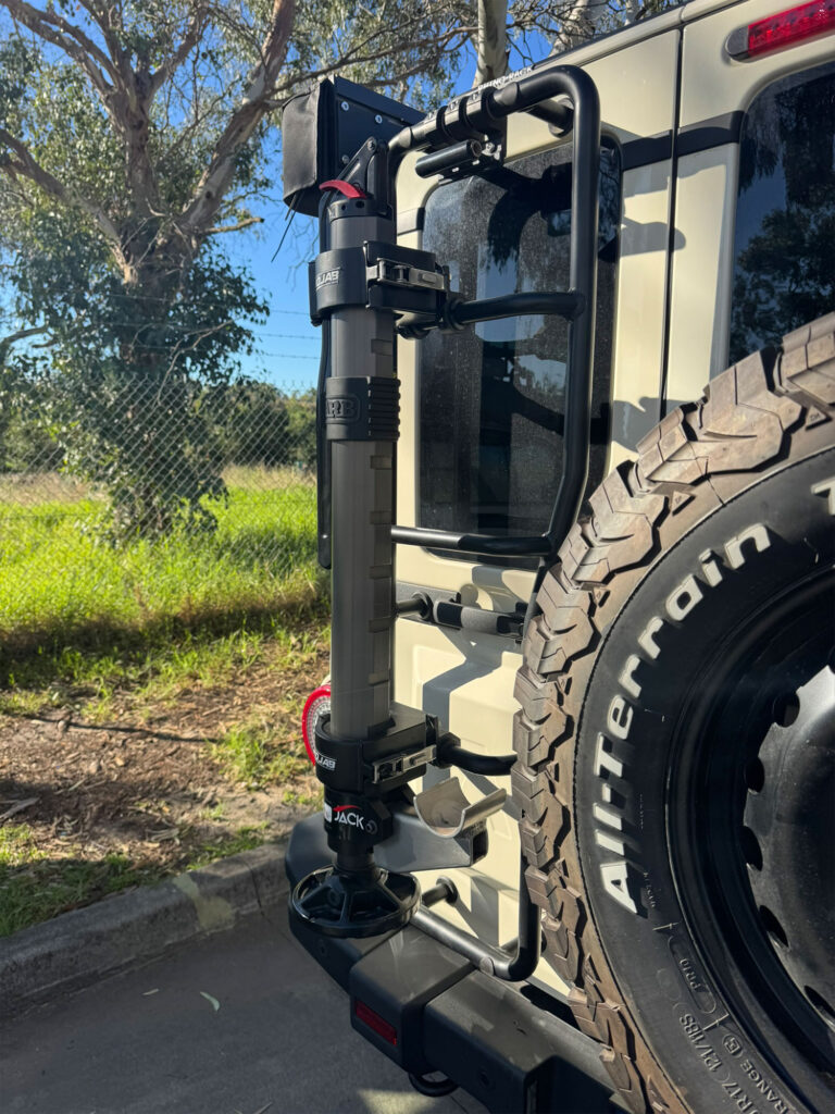 A specialized vertical exterior bracket holds the hydraulic lifting tool securely next to the spare tyre