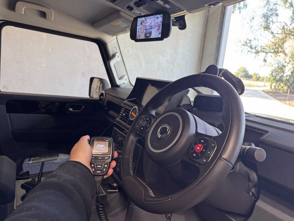 GME XRS-375C OLED controller microphone held in the driver position, displaying active communications alongside the Safety Dave mirror display feed